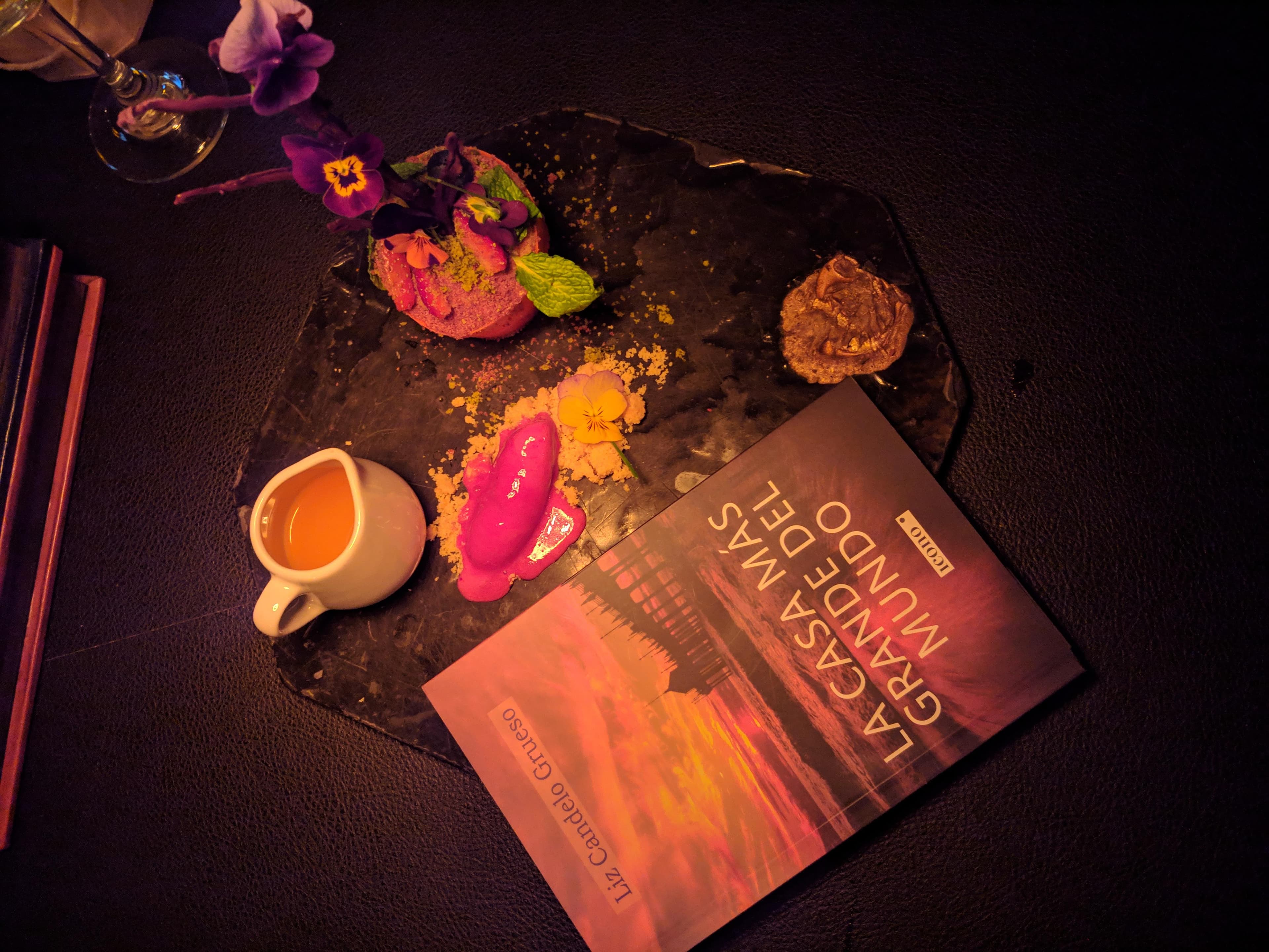 Mesa con el poemario «La Gramática de los Mundos» de Liz Candelo Grueso, flores y un jarro rosa